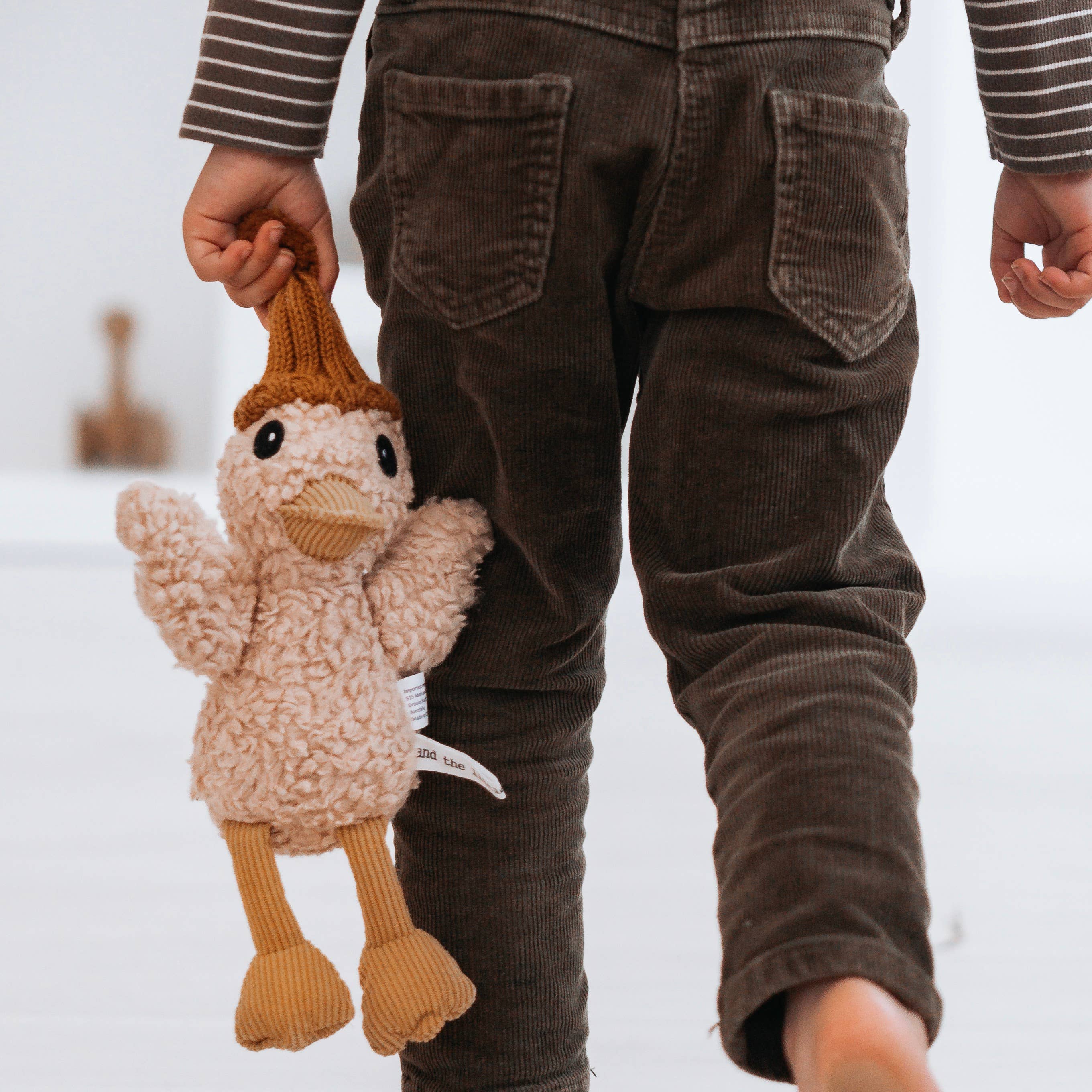 Child holding a knitted duck toy with brown pants on a white background