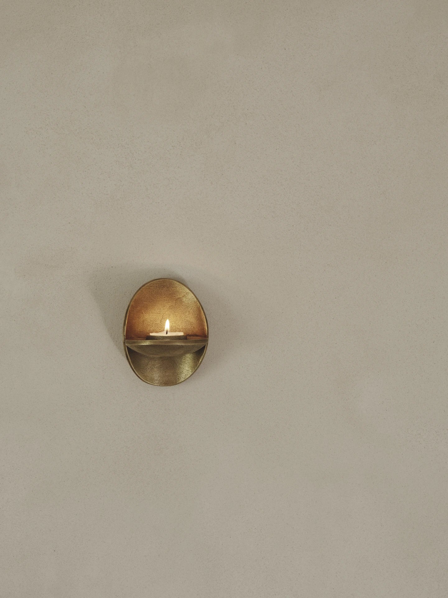 Ferm Living Agapé Wall Tealight Candle Holder Sconce in brass finish with lit candle