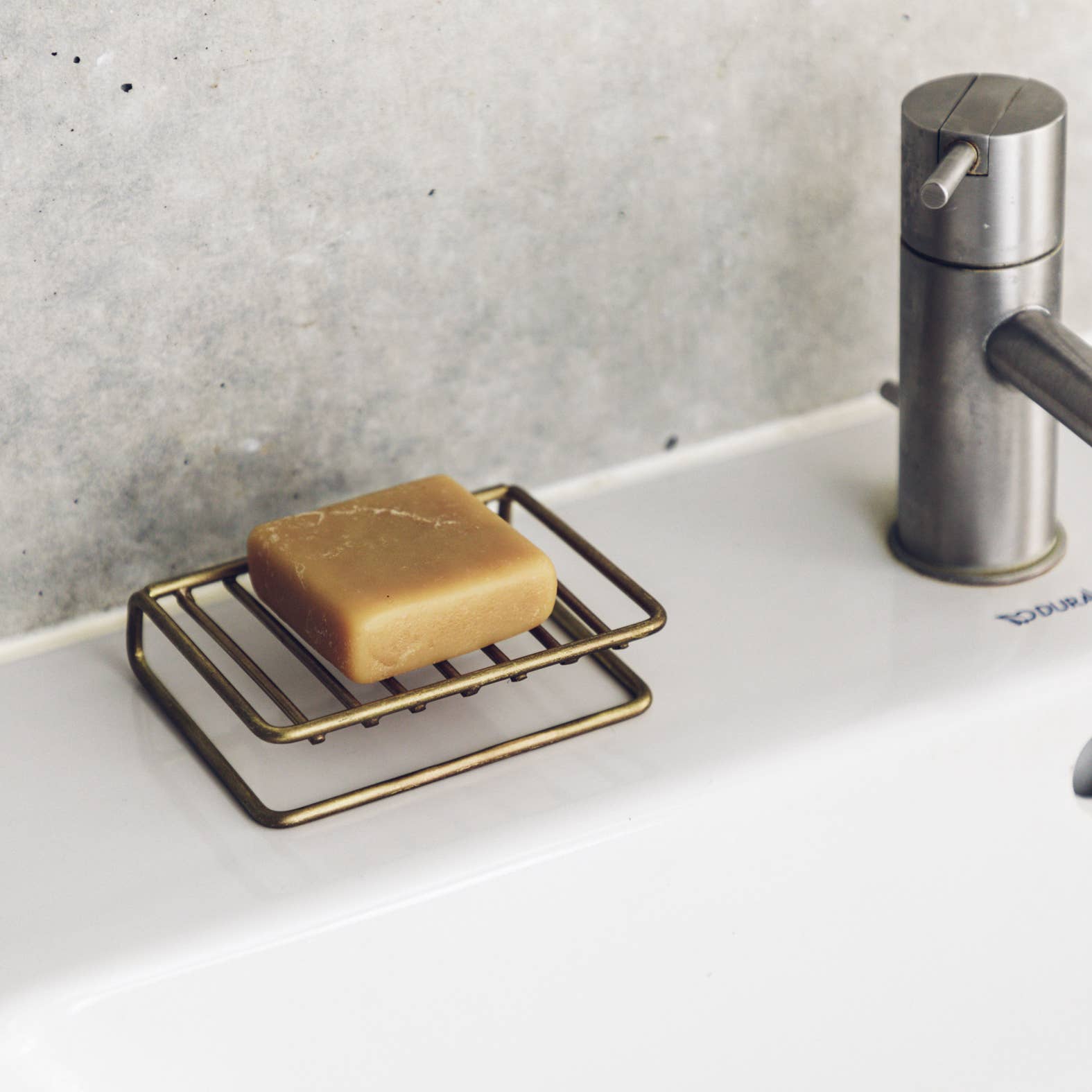 Bar of soap on a brass soap dish next to a steel tap in a bathroom setting