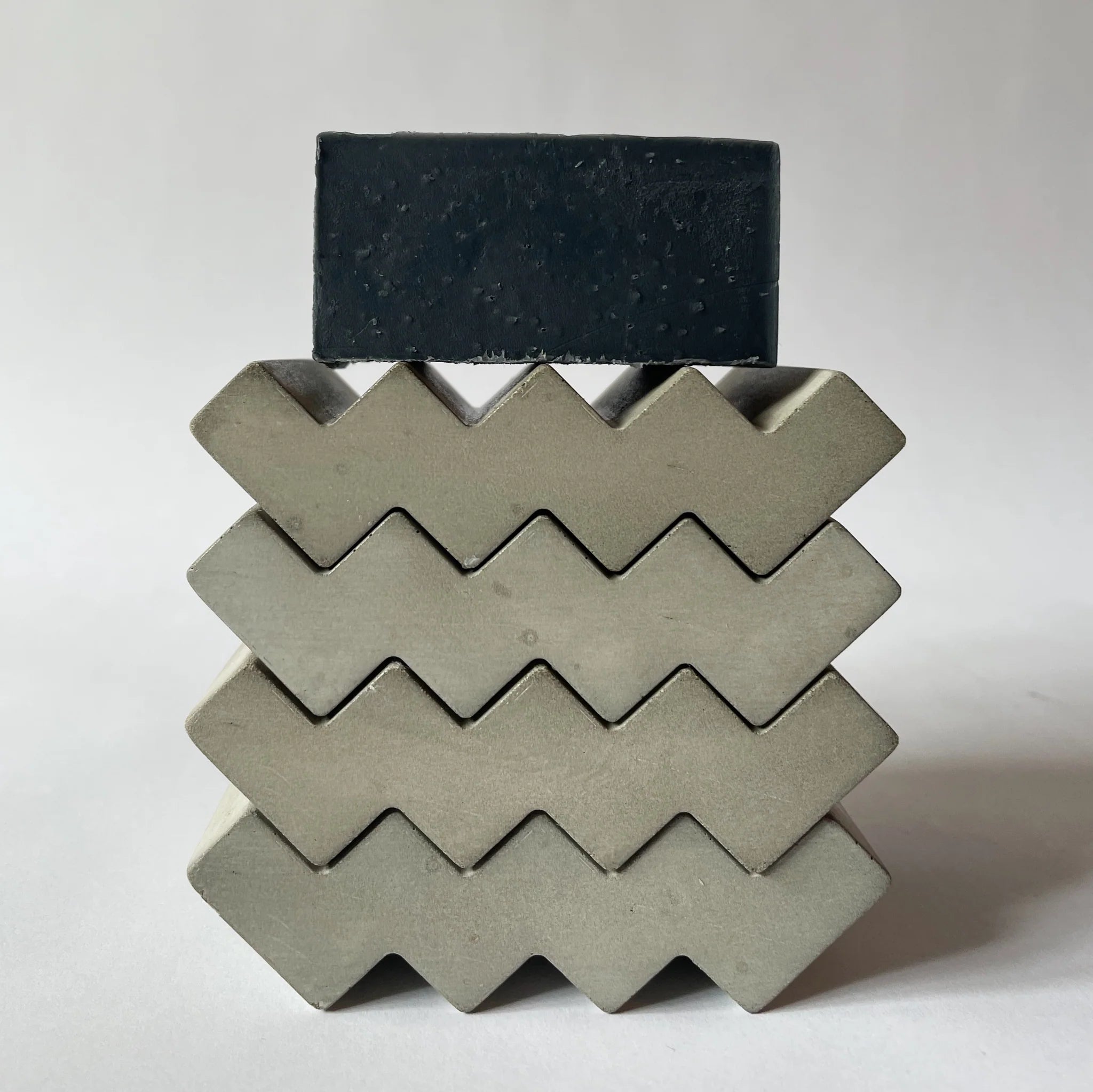 Stack of grey soap dishes in zig zag shape with a soap on top