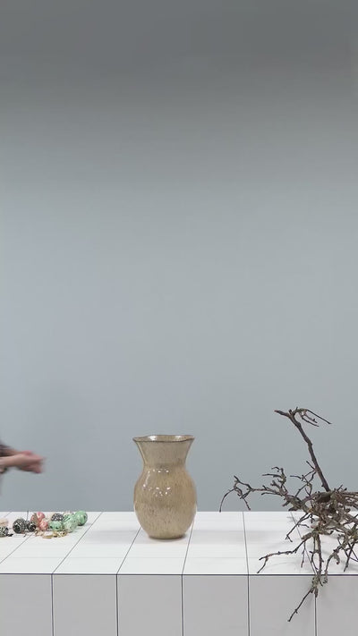 video of a woman filling a beige vase with dried branches and decorating them with easter ornaments in the shape of coloured eggs