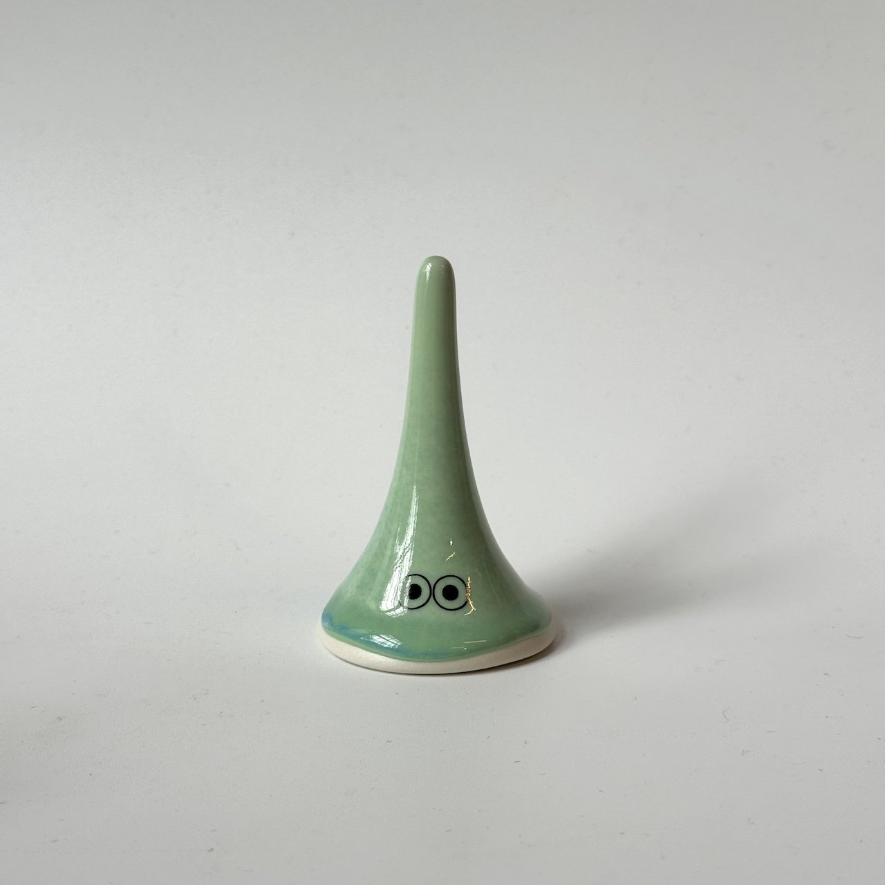 Lucy, a green Studio Arhoj familia from the Yoko family standing on a plain light grey background.