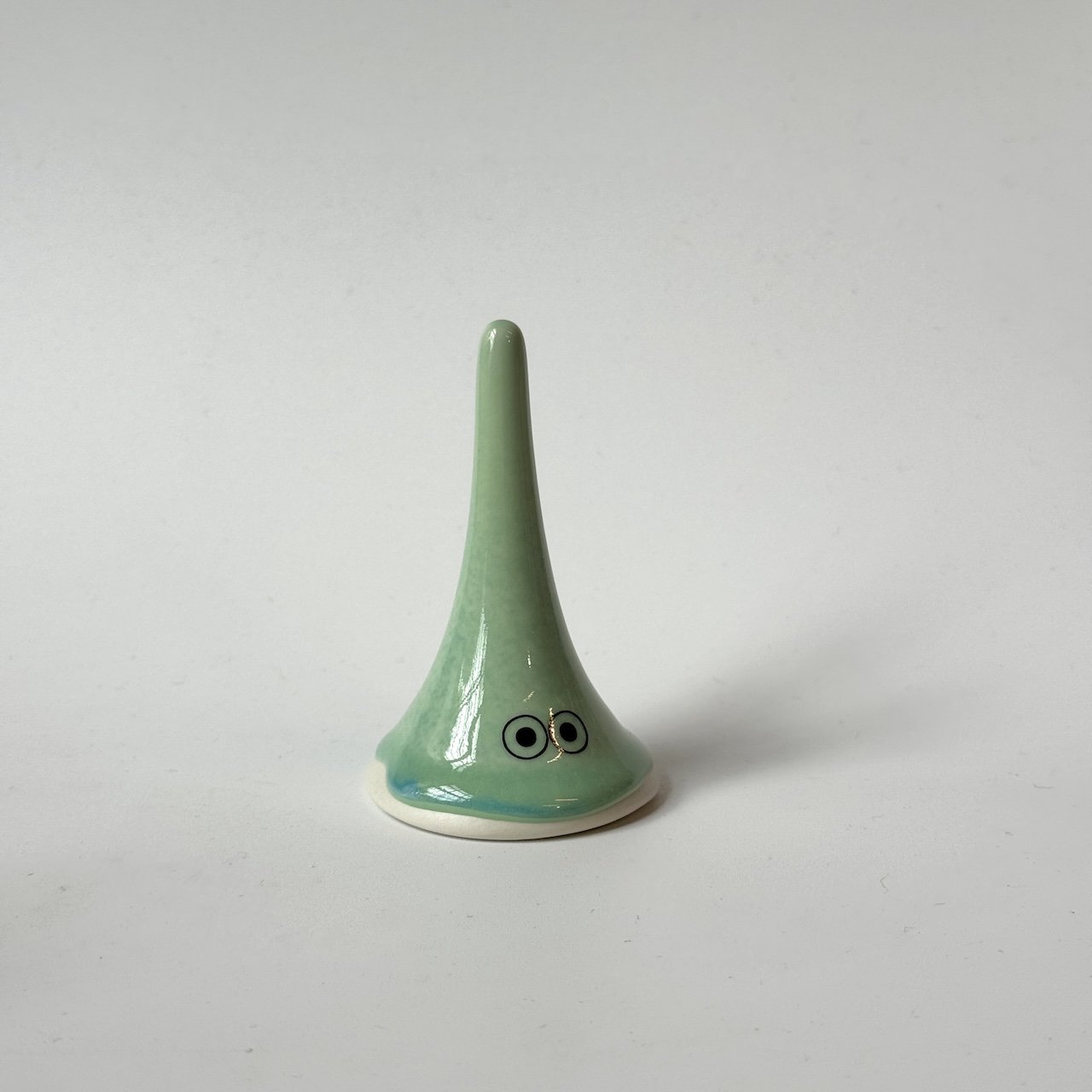 Lucy, a green Studio Arhoj familia from the Yoko family standing on a plain light grey background.